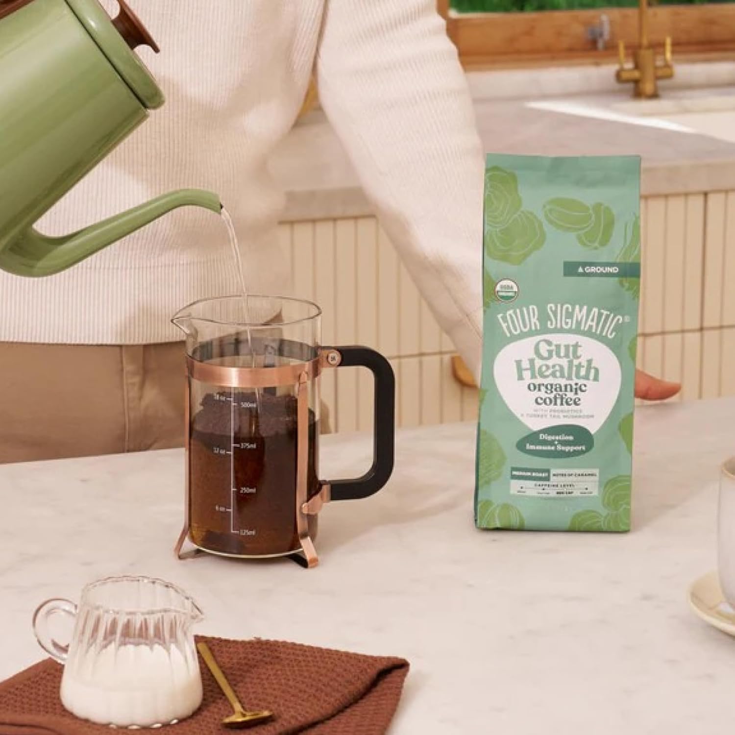How to Use: Four Sigmatic ground coffee being scooped next to a coffee maker.