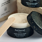Hydro ceramide cream with a wooden applicator and open lid on a white background